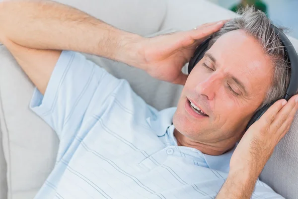 Hombre acostado en el sofá escuchando música con los ojos cerrados — Foto de Stock