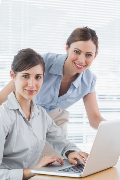 Donne d'affari sorridenti alla macchina fotografica con il computer portatile — Foto Stock