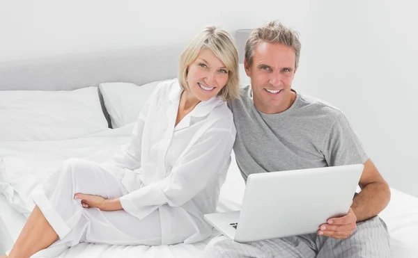 Pareja con portátil sonriendo a la cámara — Foto de Stock