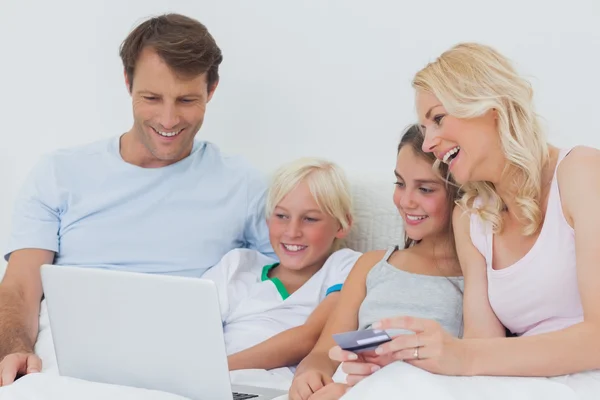 Familie nutzt Computer und Kreditkarte im Bett — Stockfoto