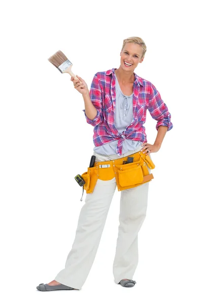 Happy woman holding paint brush wearing a tool belt — Stock Photo, Image