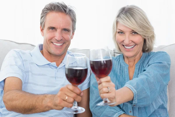 Couple toasting to the camera with red wine on the sofa — Stock Photo, Image