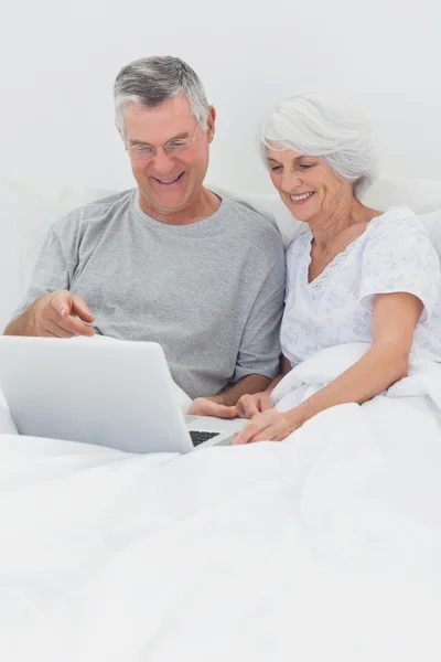 Casal usando um laptop juntos na cama — Fotografia de Stock