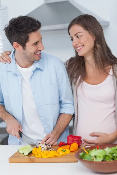 Mulher grávida olhando para o marido cortando legumes — Fotografia de Stock