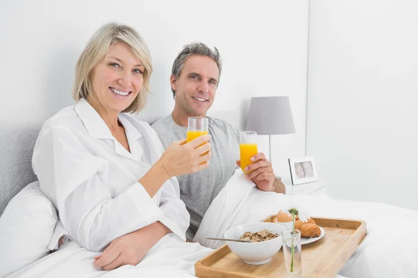 Pareja feliz tomando jugo de naranja en el desayuno en la cama — Foto de Stock