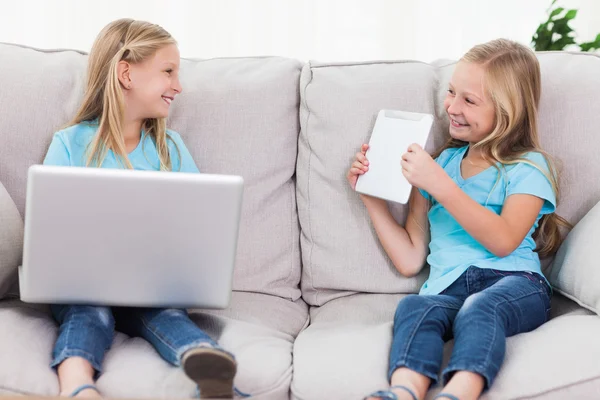 Unga tvillingar med en laptop och en tablett som sitter på en soffa — Stockfoto