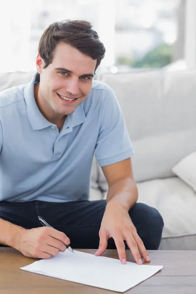 Portrait of a man writing on a paper while he is sat on a couch Stock Picture