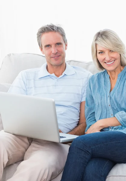 Couple using laptop together on the couch smiling at camera Stock Photo