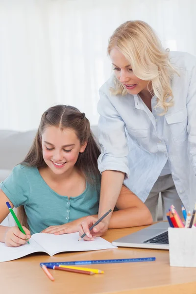 Little girl writing on a book while her mother is helping her Stock Image