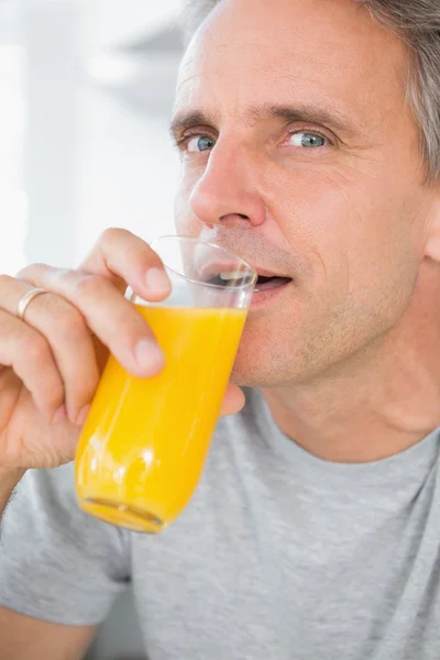 Cheerful man drinking orange juice in kitchen — Stock Photo, Image