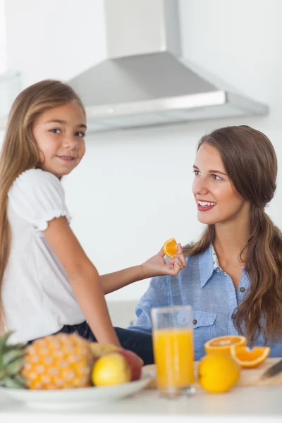 Menina bonito dando um segmento laranja para sua mãe — Fotografia de Stock