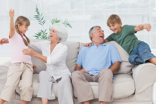 Внуки прыгают на диване со своими бабушкой и дедушкой — стоковое фото