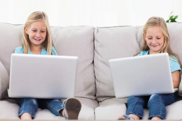 Gemelos jóvenes usando computadoras portátiles sentados en un sofá —  Fotos de Stock