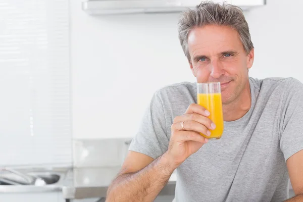 Uomo sorridente che ha un bicchiere di succo d'arancia in cucina — Foto Stock