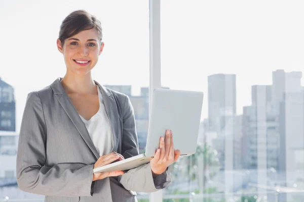 Businesswoman holding laptop and smiling at camera — Stock Photo, Image