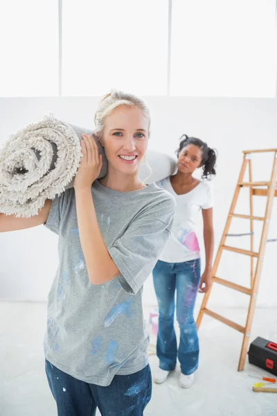 Fröhliche Mitbewohner mit zusammengerolltem Teppich im neuen Zuhause — Stockfoto