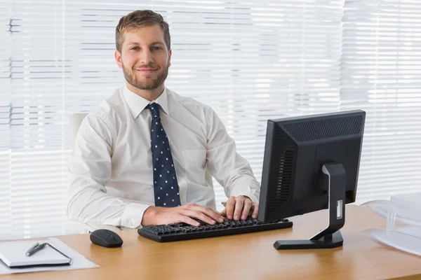 Geschäftsmann sitzt lächelnd am Schreibtisch — Stockfoto