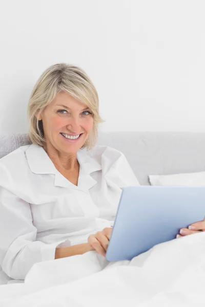 Vrolijke vrouw zitten in bed met behulp van tablet pc camera kijken — Stockfoto