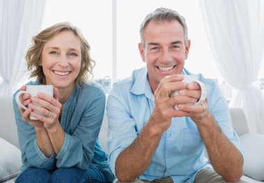 Smiling middle aged couple sitting on the couch having coffee clipart