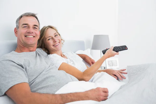 Glückliches Paar kuschelt im Bett vor dem Fernseher — Stockfoto