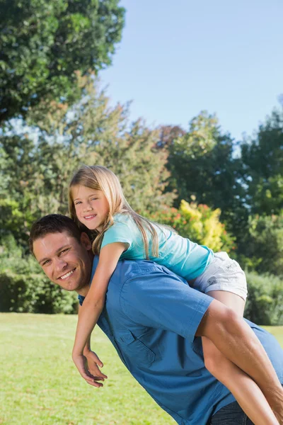 Daughter getting piggy back from dad smiling at camera — Stock Photo, Image