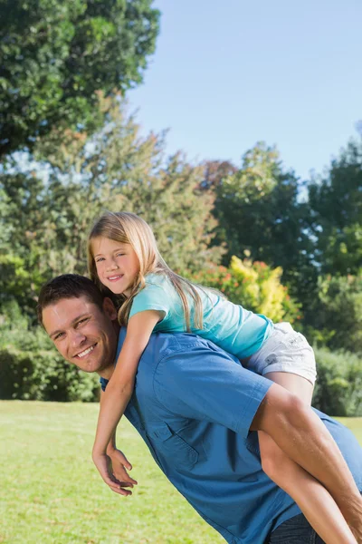 Tochter bekommt Huckepack von Papa zurück, der in die Kamera lächelt — Stockfoto