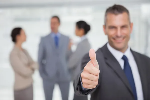 Sorrindo gerente mostrando polegar para cima com os funcionários em segundo plano — Fotografia de Stock