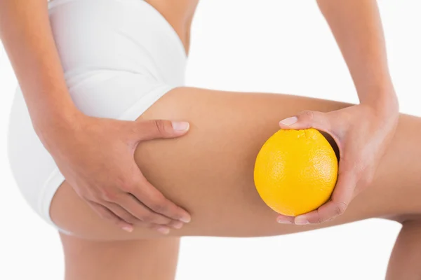 Femme mince serrant la peau de cellulite sur la cuisse comme elle tient orange — Photo