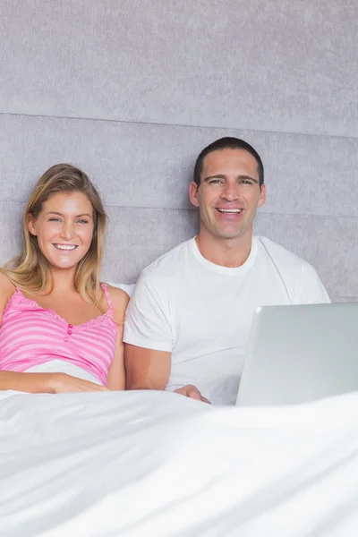 性格开朗的年轻夫妇，一起在床上使用其笔记本电脑 — 图库照片