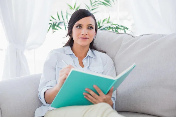 Pensive gorgeous brunette writing while sitting on the sofa — Stock Photo, Image