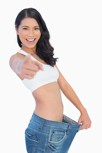 Victorious woman holding her too big pants and pointing out at c — Stock Photo, Image
