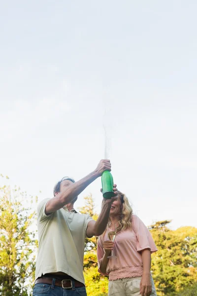 Man spraying bottle of champagne with blonde partner — Stock Photo, Image