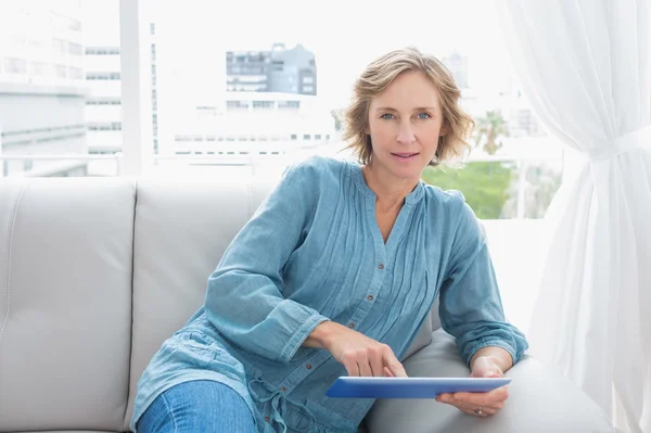 Mulher loira relaxando em seu sofá usando seu tablet — Fotografia de Stock