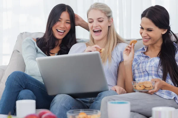 Amigos rindo olhando para laptop juntos e comer biscoitos — Fotografia de Stock