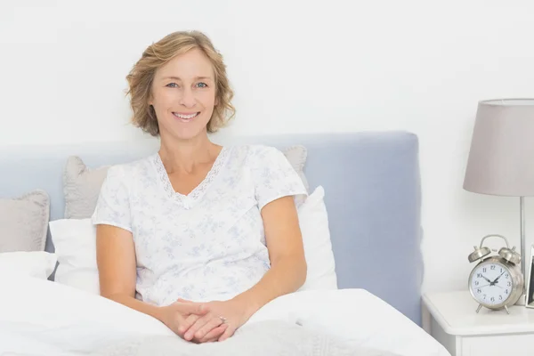 Mujer rubia sentada en la cama sonriendo a la cámara — Foto de Stock