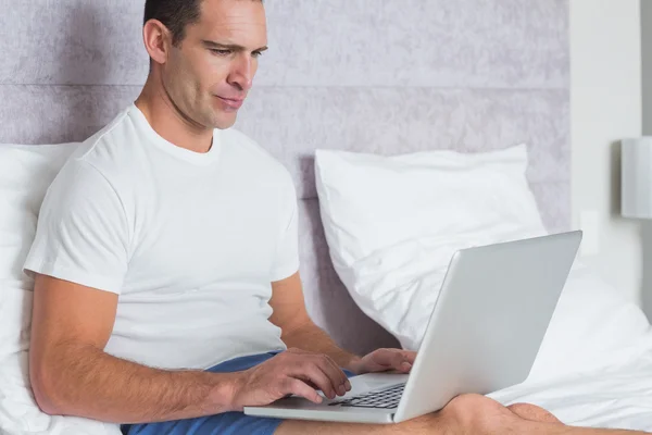 Homem sério usando laptop na cama — Fotografia de Stock