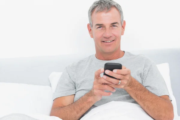 Alegre homem de cabelos grisalhos enviando um texto na cama — Fotografia de Stock