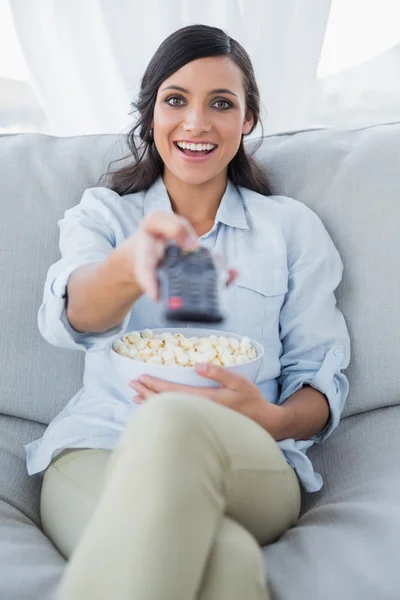 Joyeux jolie brune regarder la télévision et manger du maïs pop — Photo