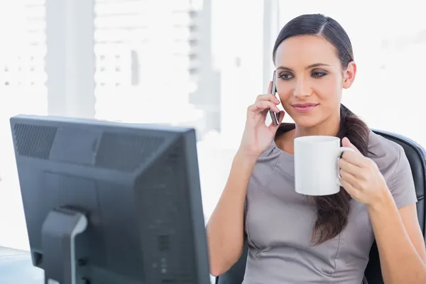 Attractive businesswoman holding coffee and answering phone — Stock Photo, Image