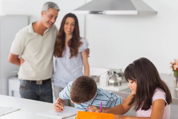 Cute siblings drawing together in kitchen with their parents smi — Stock Photo, Image