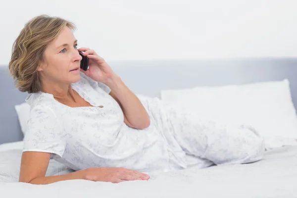 Mujer rubia seria acostada en la cama haciendo una llamada telefónica — Foto de Stock