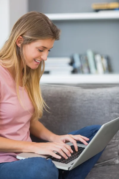 Attraktiva blonde sitter på hennes soffa med laptop — Stockfoto