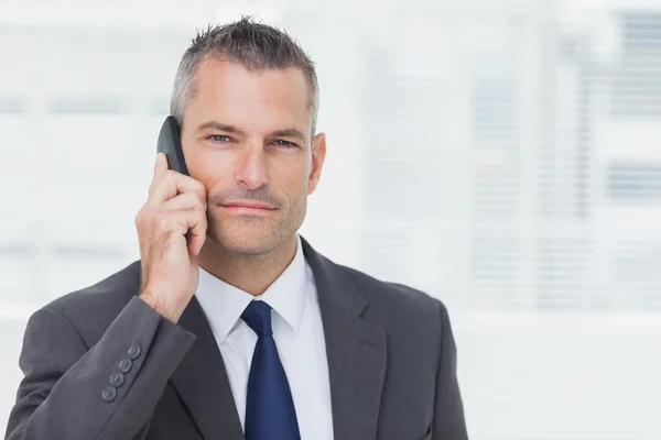 Бизнесмен смотрит в камеру во время телефонного звонка — стоковое фото