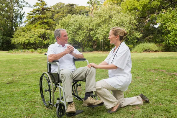 Sorrindo homem em uma cadeira de rodas falando com sua enfermeira besi ajoelhado — Fotografia de Stock