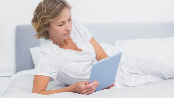 Szczęśliwy blond kobieta, leżąc na łóżku przy użyciu komputera typu tablet — Zdjęcie stockowe