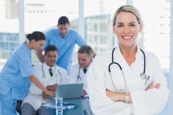 Sonriente médico rubio posando con colegas de fondo —  Fotos de Stock
