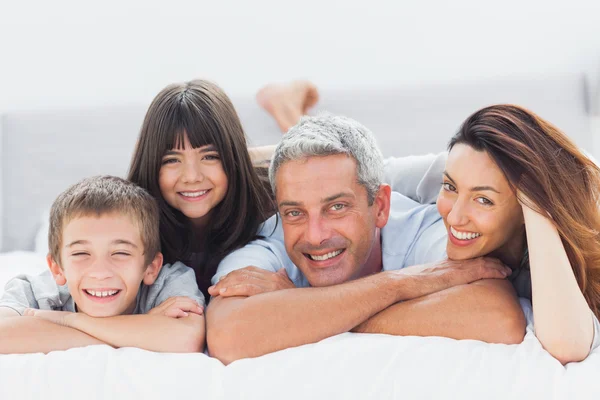 Nette Familie liegt auf dem Bett und lächelt in die Kamera — Stockfoto