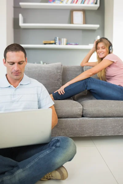 Мужчина сидит на полу, используя ноутбук с женщиной, слушающей музыку — стоковое фото