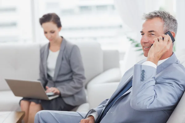 Бизнесмен разговаривает по телефону, пока его коллега работает над ее лаптом — стоковое фото