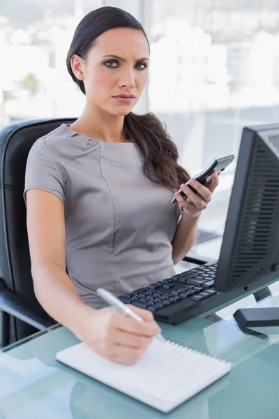 Annoyed businesswoman using calculator and writing — Stock Photo, Image